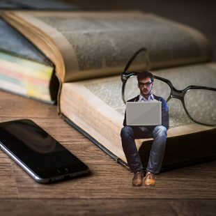 Image d'un livre, de lunettes et teléphone et un petit homme asis sur le livre un ordinateur sur les genoux
