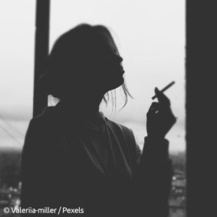 photographie en noir et blanc d'une femme à contrejour en train de faire une pause avec une cigarette