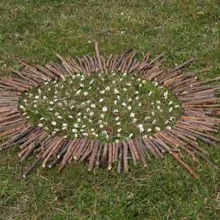 Photographie d'une oeuvre de land art batons et pierres posés en cercle dans l'herbe