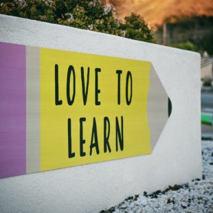 Panneau en forme de crayon "love to learn" avec un homme marchant à côté