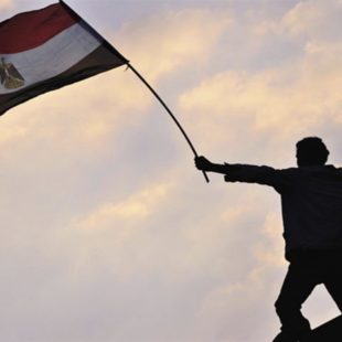 Homme debout dans le crépuscule, levant le drapeau égyptien