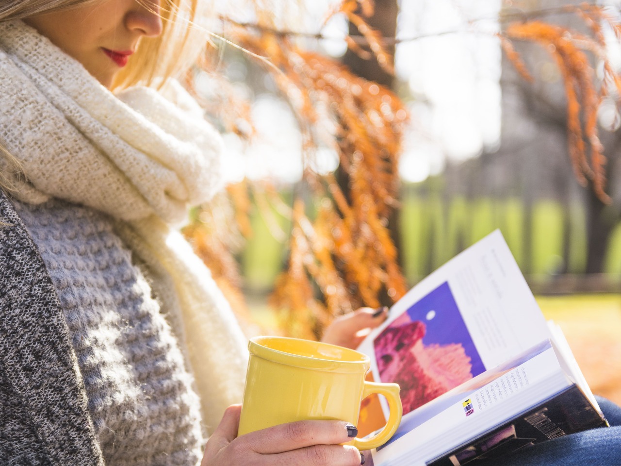 Femme en train de lire à l'extérieur avec une tasse.