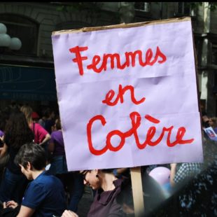 Manifestation de femmes dans une rue. Au premier plan est brandie une pancarte sur lequel est inscrit Femmes en colère
