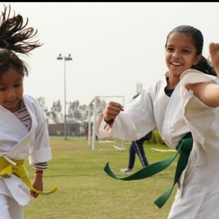 Deux jeunes filles qui portent la ceinture verte faisant du karaté à l'extérieur sur un terrain de foot