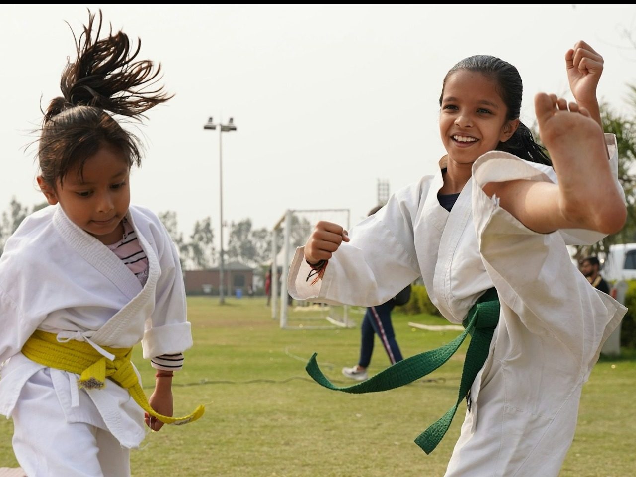 Deux jeunes filles qui portent la ceinture verte faisant du karaté à l'extérieur sur un terrain de foot