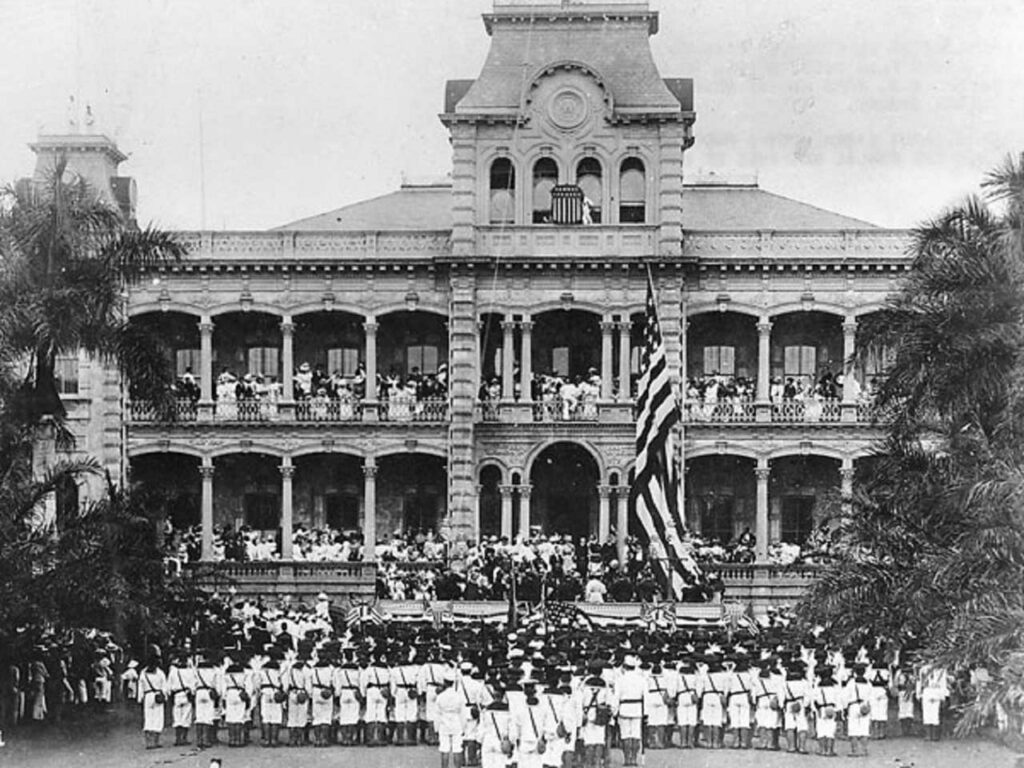 Levée du drapeau américain lors de la cérémonie d'annexion des États-Unis au Palais ʻIolani, à Honolulu, Hawaï. Les marines américains qui participent à la cérémonie appartiennent à l'USS Philadelphia. Collection : Collection Ray Jerome Baker.