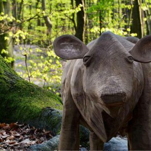 Scupture d'une vache en bois au milieu d'une forêt