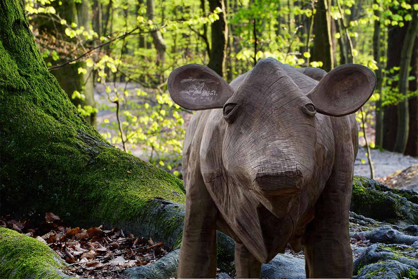 Scupture d'une vache en bois au milieu d'une forêt