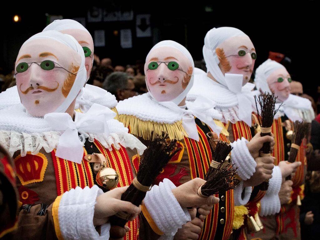 Photographie en couleurs de format paysage composée de 5 personnages costumés (rassemblement des Gilles) dans une foule. Les personnages au premier plan sont cadrés en plan poitrine. La photographie est très colorée.