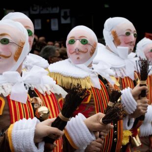 Photographie en couleurs de format paysage composée de 5 personnages costumés (rassemblement des Gilles) dans une foule. Les personnages au premier plan sont cadrés en plan poitrine. La photographie est très colorée.